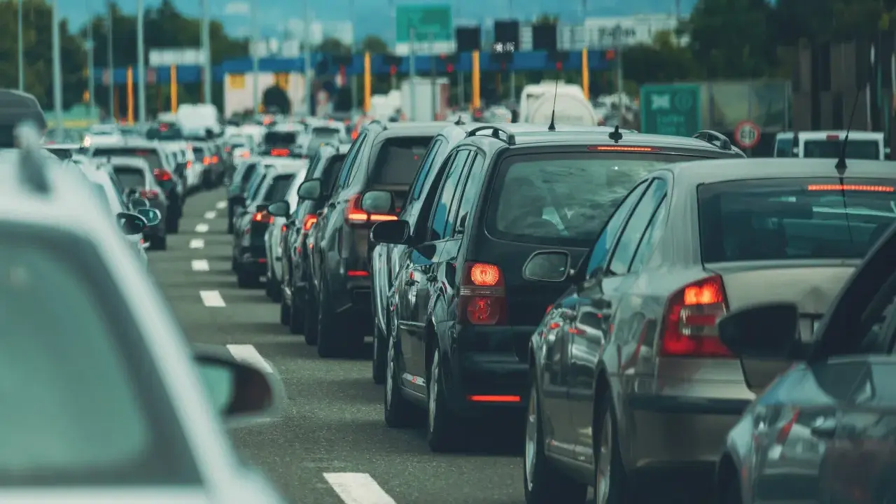 Korki na autostradzie, rząd samochodów. W tle widać bramki opłat i znaki drogowe, które mogą nawiązywać do normy emisji spalin tabela.