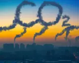 Dym z kominów układa się w napis "CO2", symbolizując globalną emisję dwutlenku węgla nad miastem o zachodzie słońca.