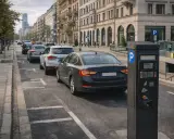 Czarny parkometr na tle ulicy z zaparkowanymi samochodami i budynkami.