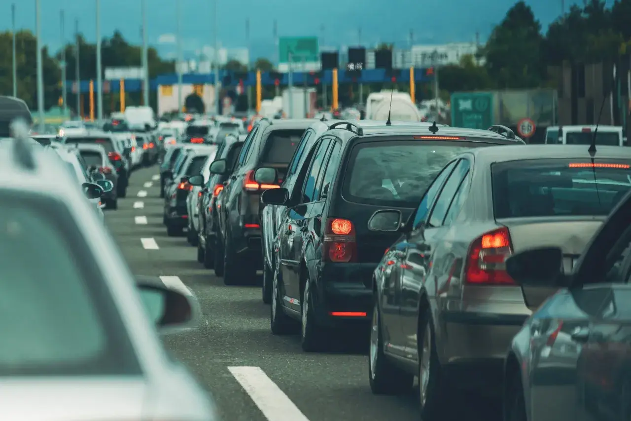 Korki na autostradzie, rząd samochodów. W tle widać bramki opłat i znaki drogowe, które mogą nawiązywać do normy emisji spalin tabela.